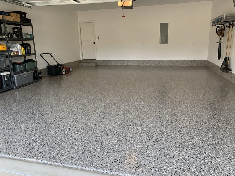 Finished flake floor in a garage with storage shelves, a lawn mower and wall-mounted tools